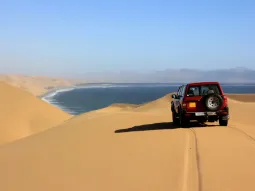 Czerwony samochód terenowy 4x4 na wydmach Sandwich Harbour w Namibii, w miejscu gdzie pustynia Namib spotyka Ocean Atlantycki.