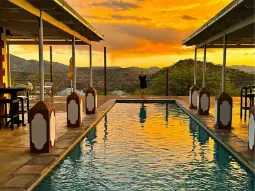 Kobieta stojąca na tarasie lodge patrząca na zachód słońca. Przed nią basen i podcienia lodge w Namibii.