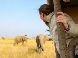 Widok z boku na przód białego samochodu terenowego 4x4 (typu Land Rover Defender) z podwyższonym wlotem powietrza, stojącego na krawędzi wysokiej piaszczystej wydmy. W dole rozciąga się wąski pas plaży, gdzie pustynia Namib styka się z ciemnoniebieskimi wodami Oceanu Atlantyckiego pod bezchmurnym niebem.