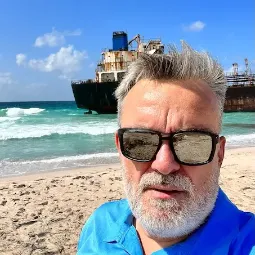 Jarek Skowron, polski pilot i przewodnik safari z outventure.life, na surowym tle osadzonego na plaży wraku statku. Idealna sceneria dla miłośników dzikiej przyrody.