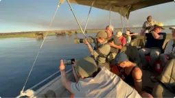 Grupa turystów na łodzi podczas rejsu safari po rzece Chobe w Botswanie, fotografująca stado słoni kąpiących się w wodzie o zachodzie słońca.